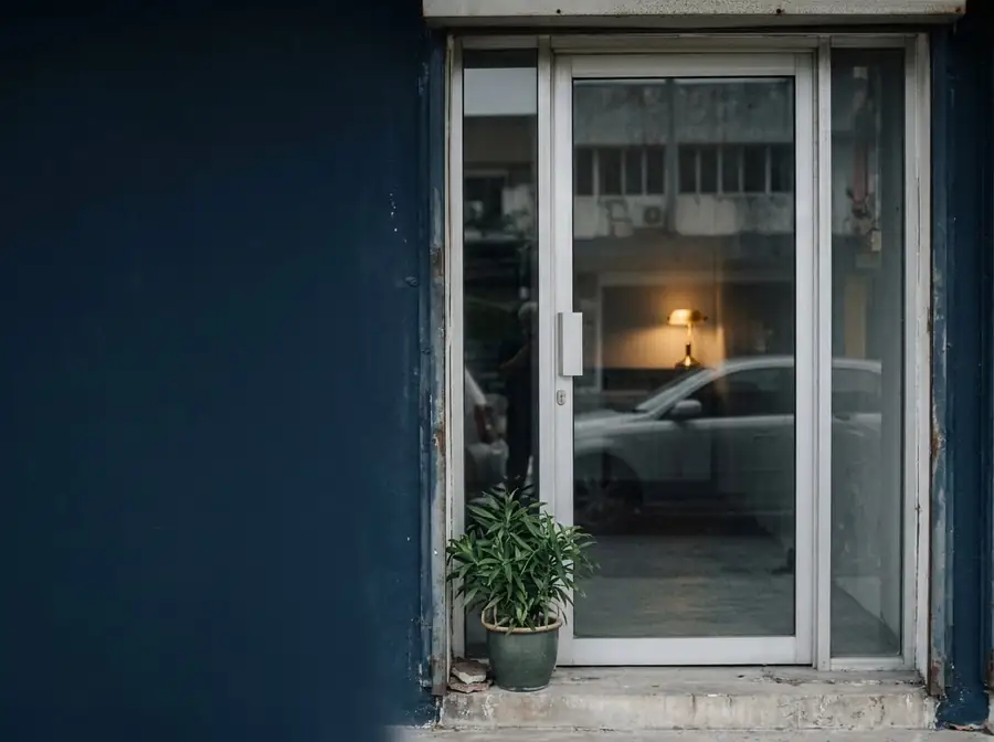 The same shop door, clean, with a healthy plant and a warm lamp inside.