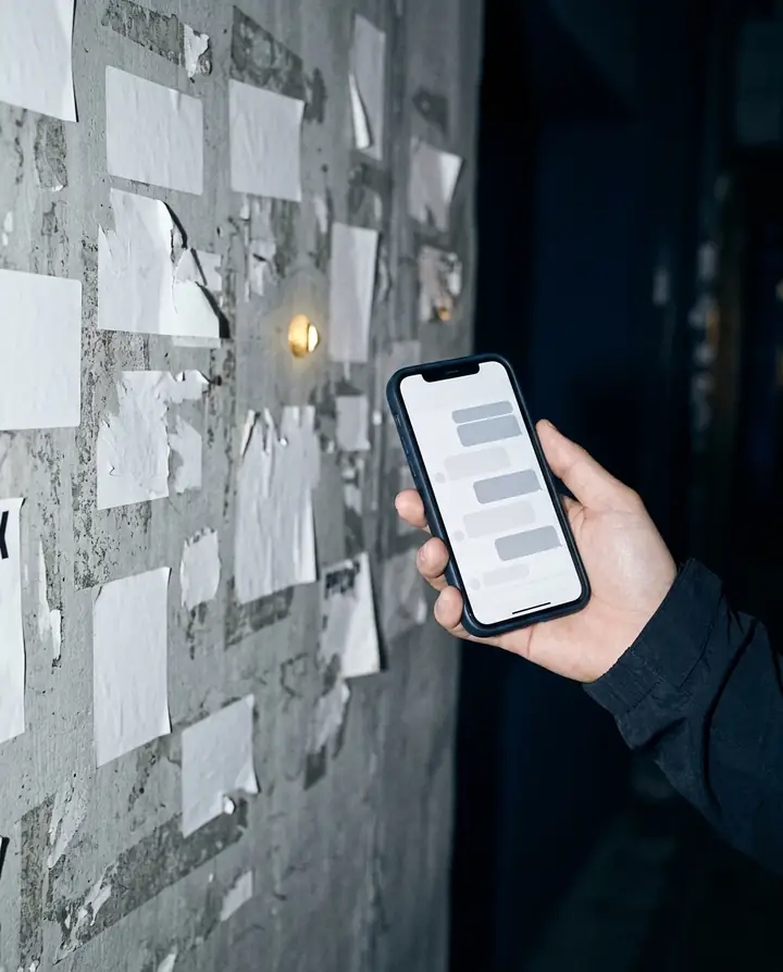 A hand holding a phone in front of a wall of blank stickers.